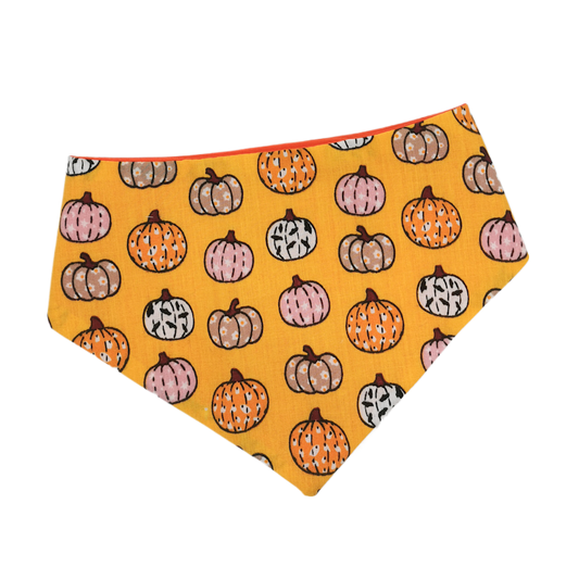 A triangular bandana for cats or dogs with an orange background featuring a pattern of variously colored pumpkins, perfect for Halloween