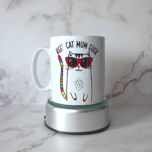 Photo shows a mug with "Best Cat Mum Ever" over a cute cat wearing sunglasses with a rainbow tail, perfect gift for cat mums