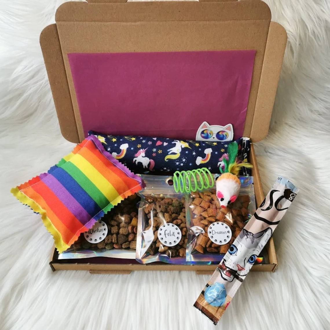 Picture shows a small cat treat gift box, with three small packs of cat treats, a catnip kicker and pillow, a cat treat stick and two toys