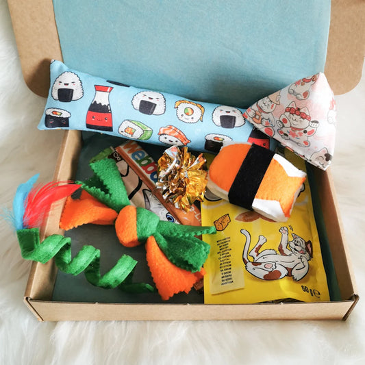 Picture shows a sushi themed cat gift box with a catnip kicker, triangle and felt nigiri, with a green felt cat spring and a green and orange fleece sweet, there is also cat treats and a crinkle ball