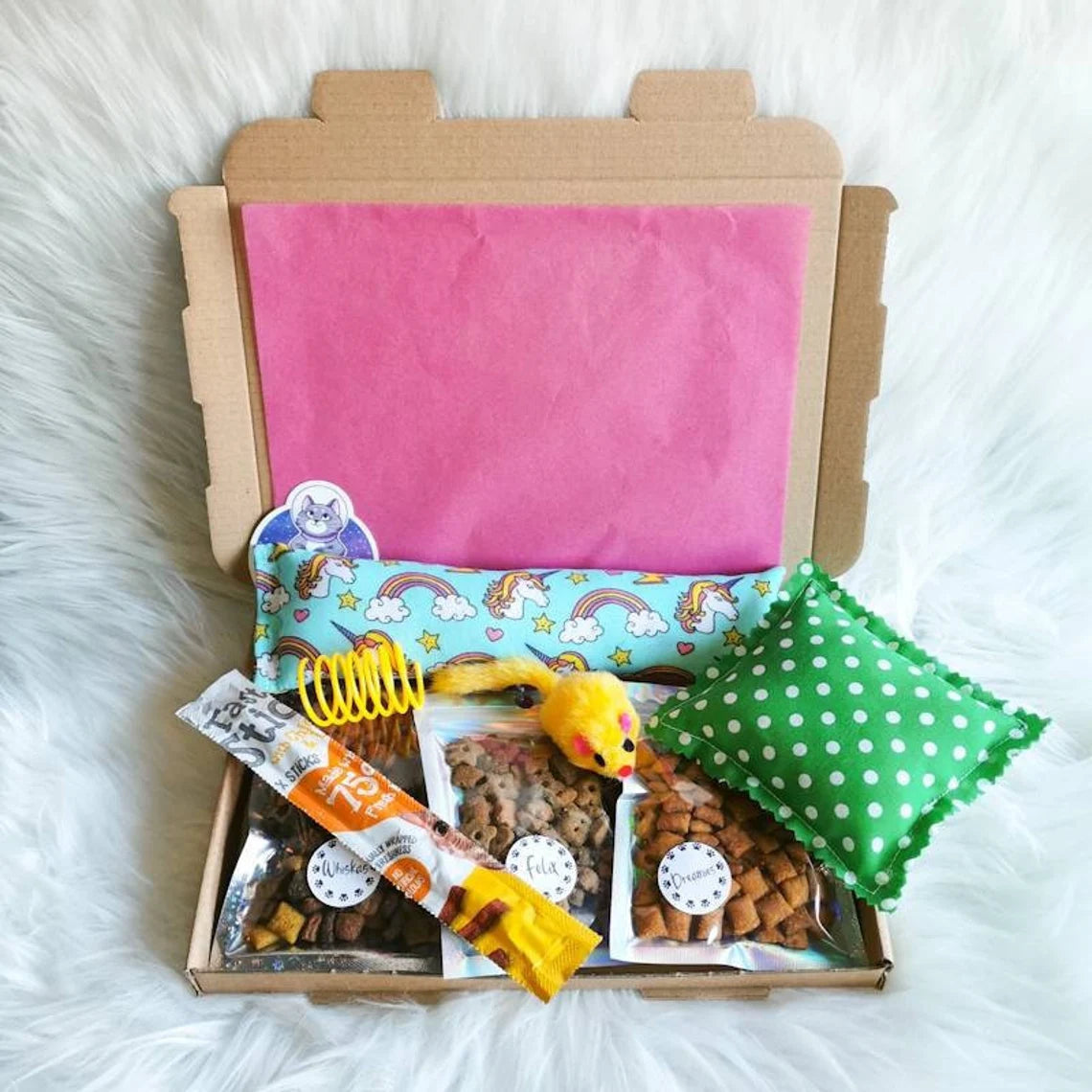 Picture shows a small cat treat gift box, with three small packs of cat treats, a catnip kicker and pillow, a cat treat stick and two toys