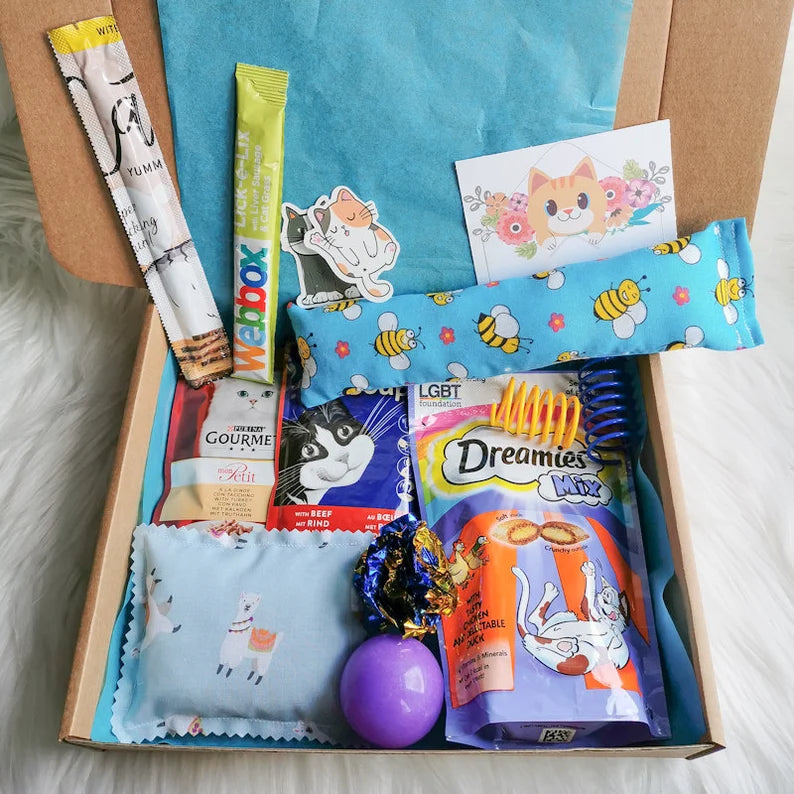 Picture shows a blue themed cat gift box with catnip kicker, pillow, two pouches of cat food, cat treats and various cat toys