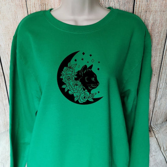 a green sweatshirt with a cat, a moon and flowers on, the sweatshirt is made from comfy and warming fabric, great for autumn and winter 