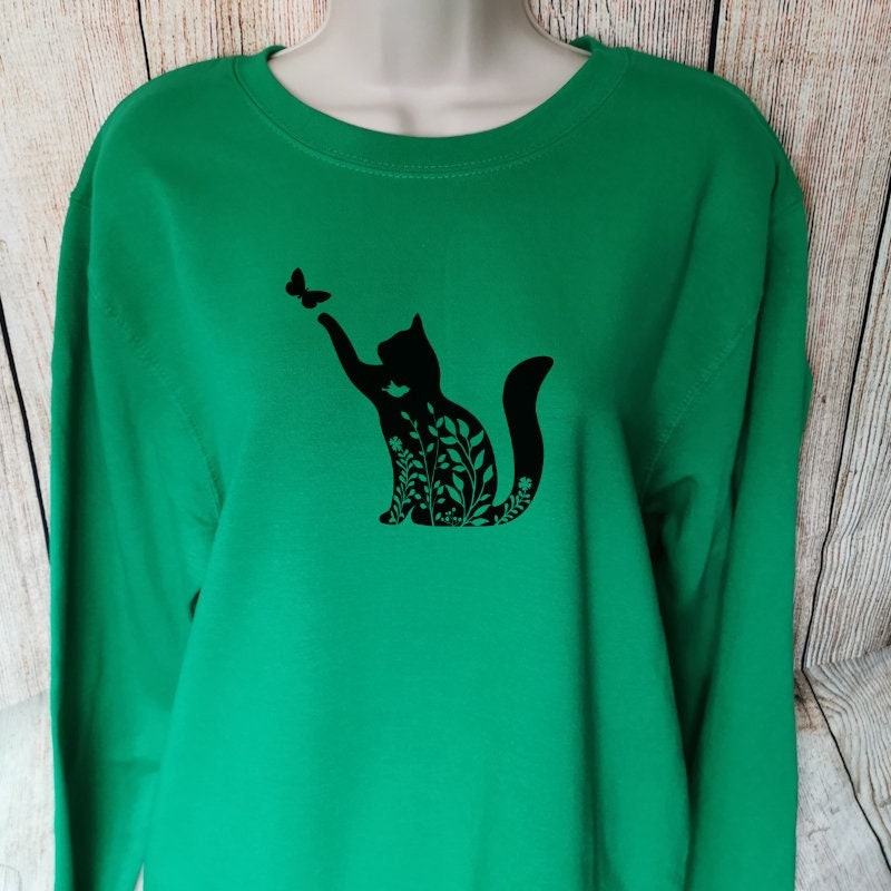 a sweatshirt for cat lovers in the colour green which has a floral cat playing with a butterfly