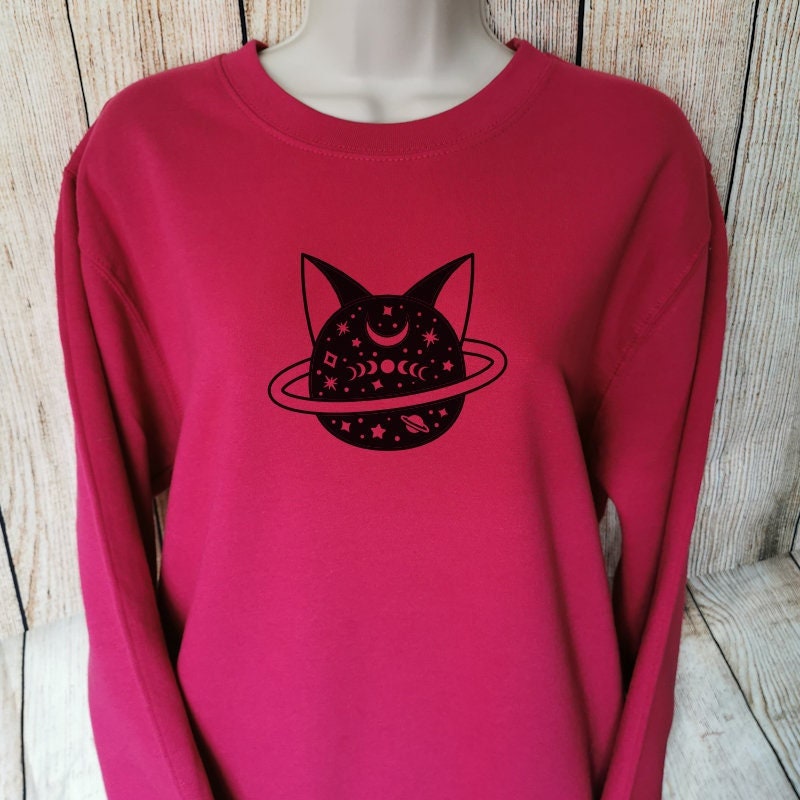 A cranberry sweatshirt which shows a cats head depicted as a planet, great gift for any cat lover 