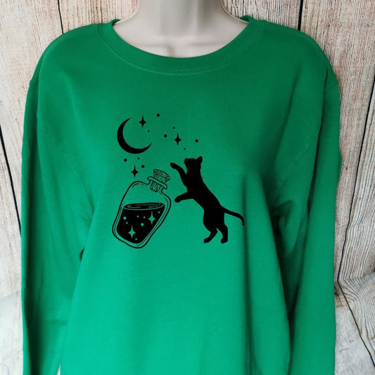 a green sweatshirt which has a black cat chasing stars that have come out of a bottle, the whimsical design makes this a perfect gift for cat lovers and fantasy lovers alike