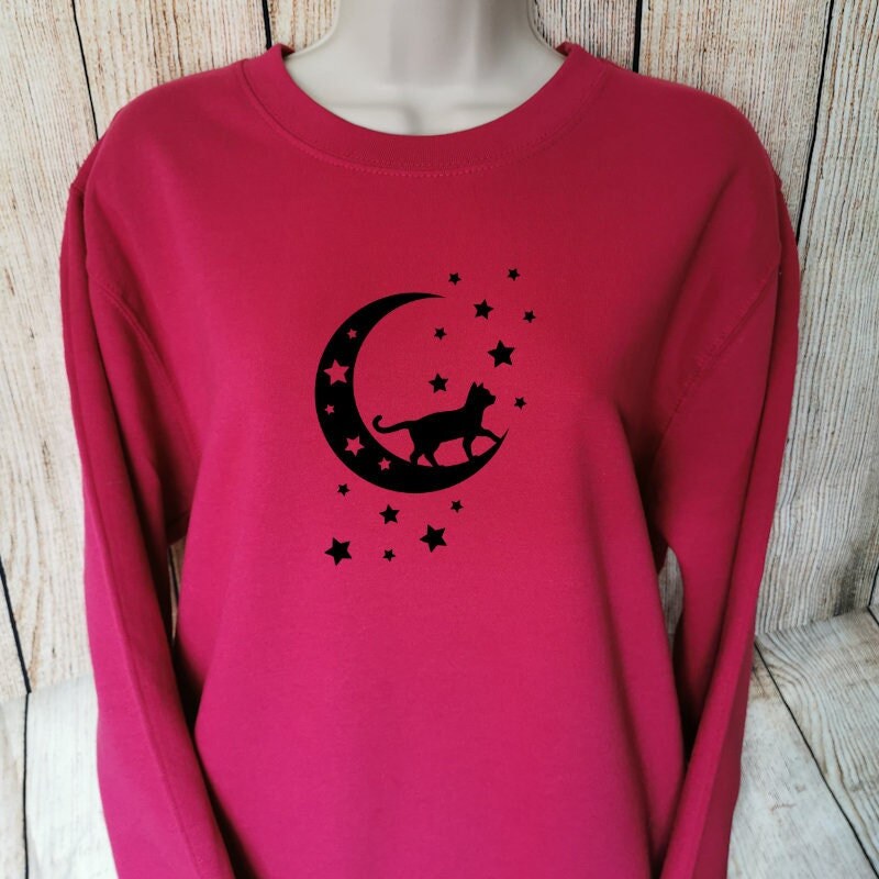 a sweatshirt for cat people in the colour cranberry which shows a cat stood on a moon looking at the stars