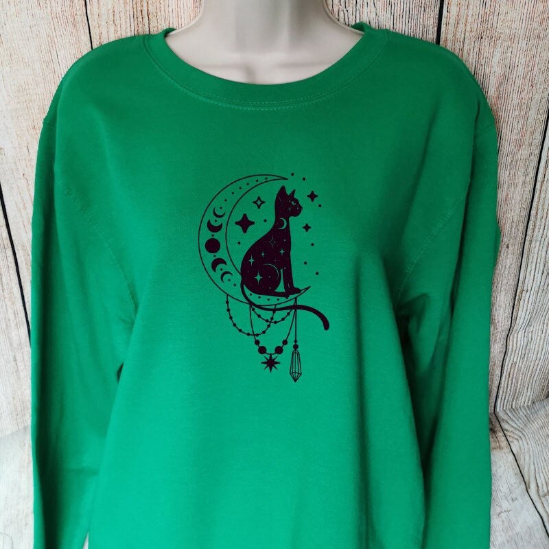 a sweatshirt for cat lovers in the colour green which has a sphynx cat sat in a moon with the moon phases on